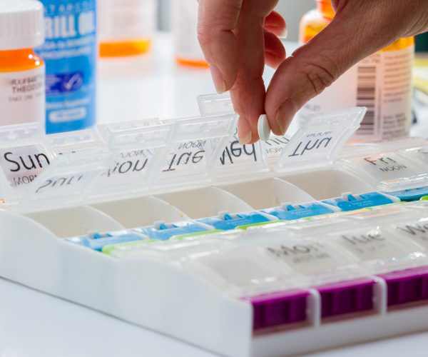 details of a hand carefully organizing prescriptions pills for a weekly dose